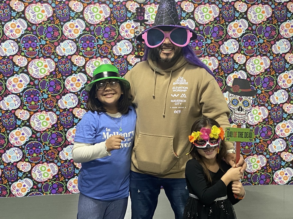 Father and daughters wearing sunglasses and holding day of the dead sign in front of Day of the Dead backdrop