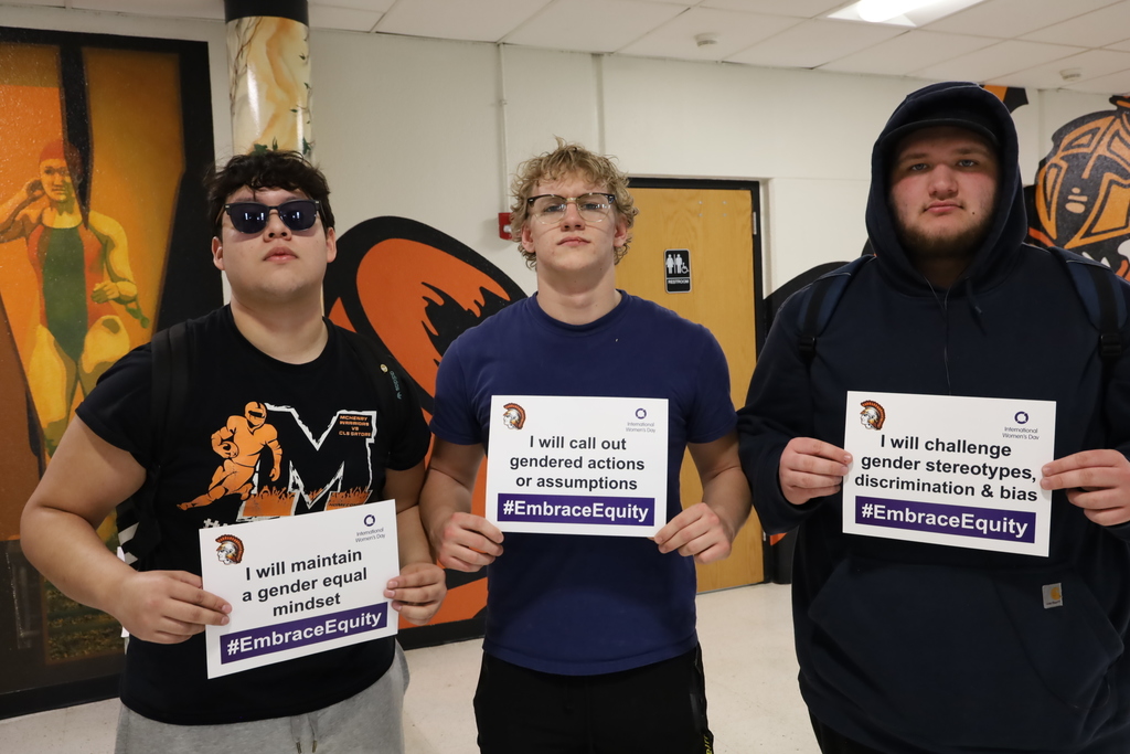 Three students holding signs that say,  "I will maintain a gender equal mindset." "I will call out gendered actions or assumptions." and "I will challenge gender stereotypes, discrimination and bias."