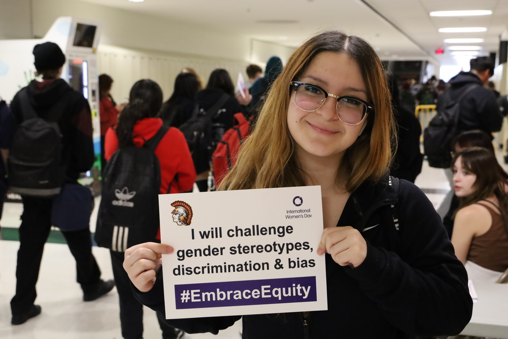 A student holding a sign that says "I will challenge gender stereotypes, discrimination and bias."