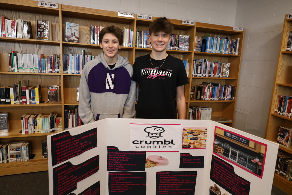 Two students in front of a Crumbl cookies poster