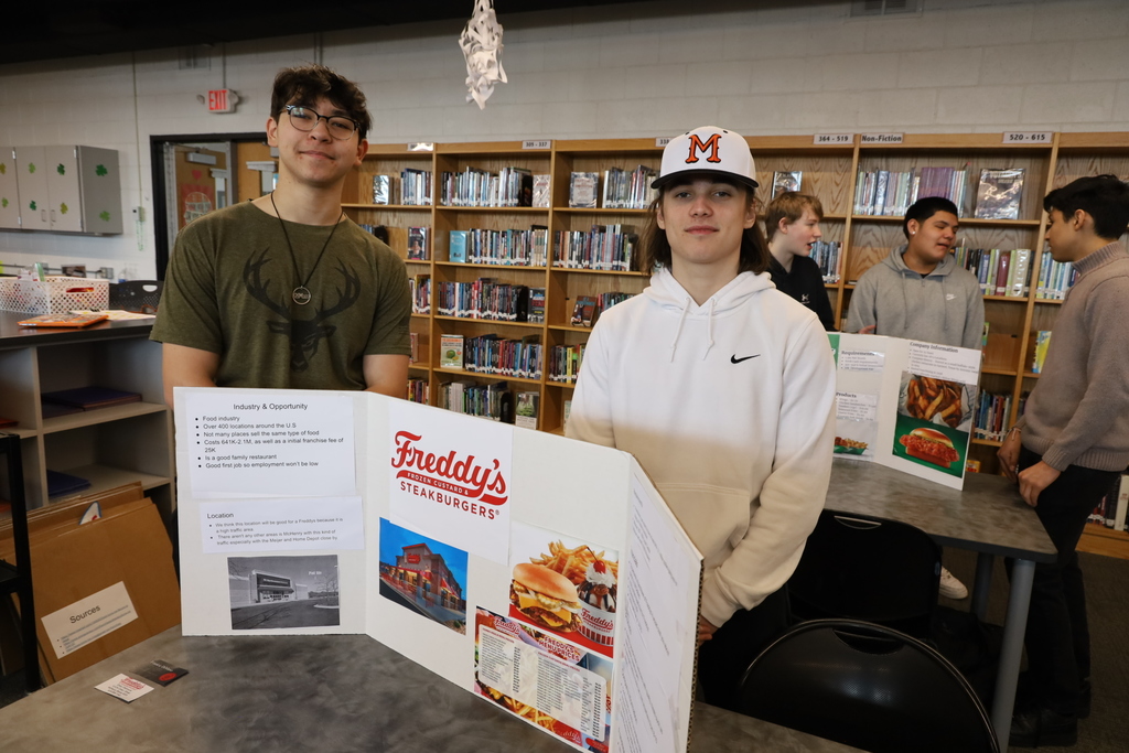 Two students standing with a Freddy's poster